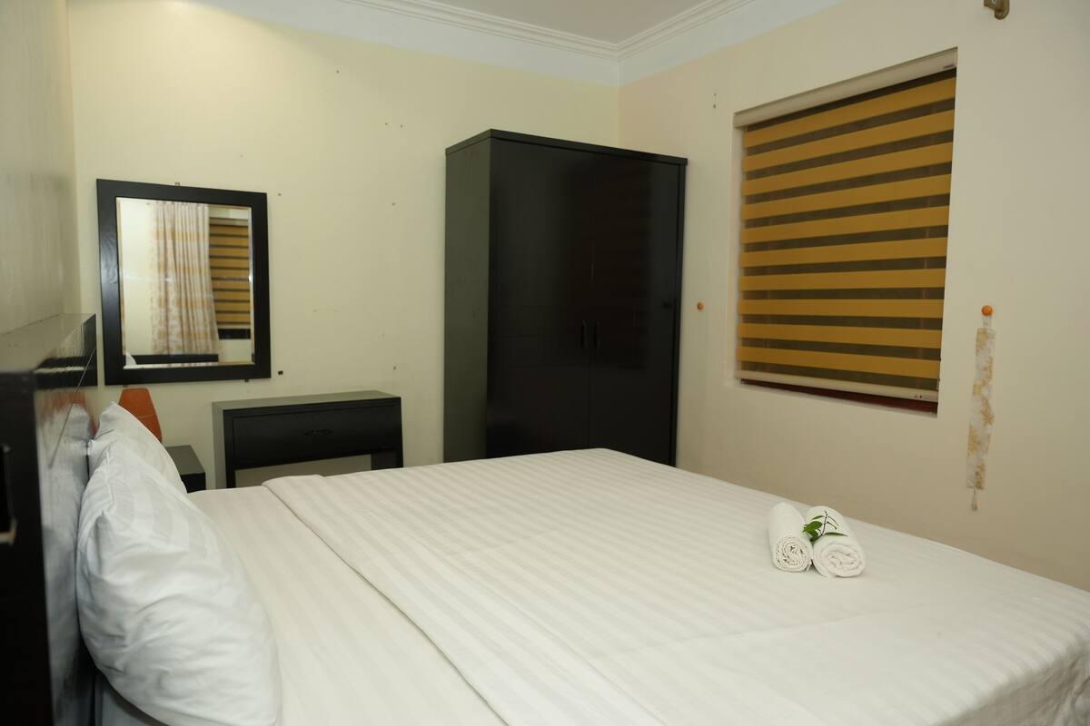 Una habitación de hotel con cama, armario, escritorio y ventana con persianas.