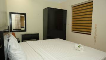Ein Hotelzimmer mit Bett, Kleiderschrank, Schreibtisch und einem Fenster mit Jalousien.