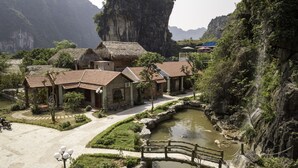 A traditional village with thatched-roof houses, a small pond, and a bridge. - Trang An Heritage Garden (Tay Hoa Lu)