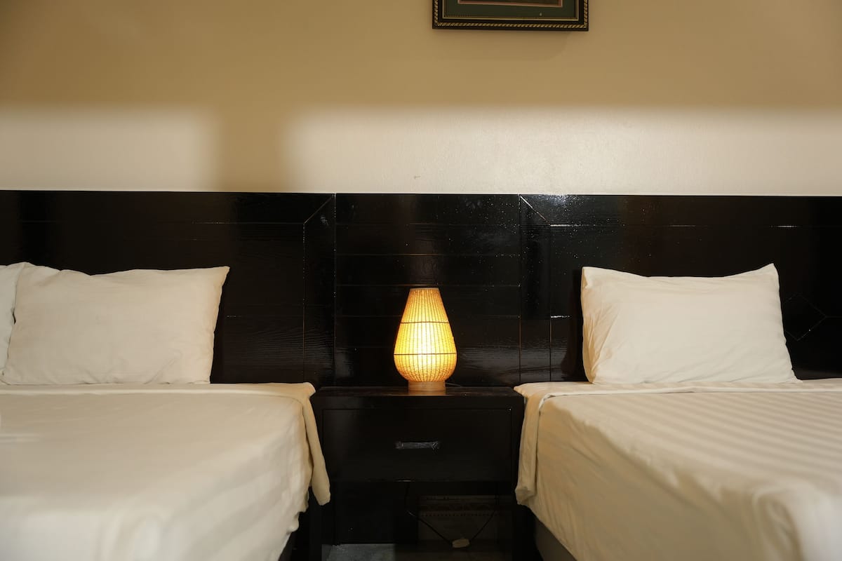 Habitación de hotel con dos camas, una mesita de noche con lámpara y un cuadro enmarcado en la pared.