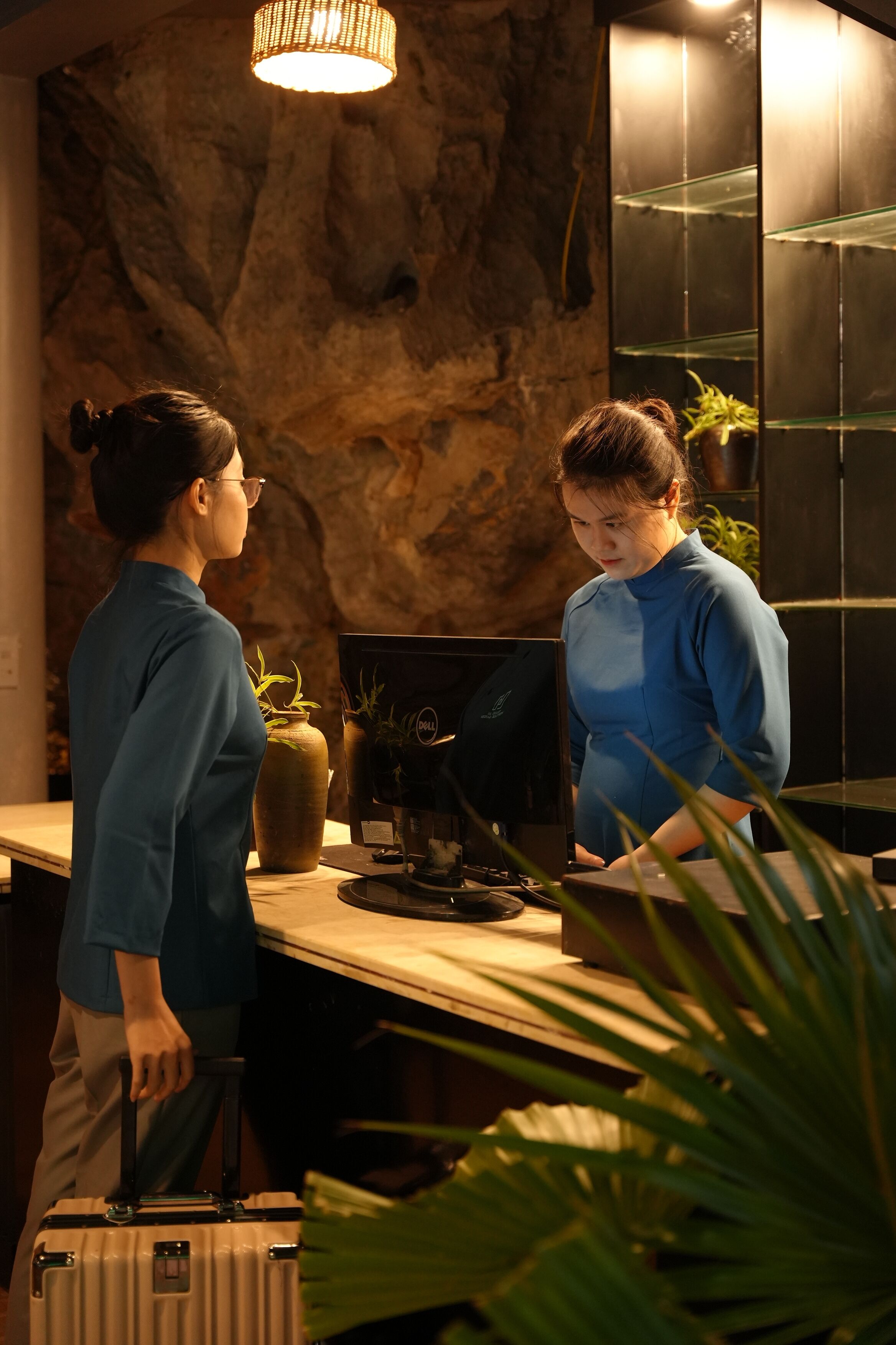 A reception desk with a stone wall backdrop, a computer, and potted plants.