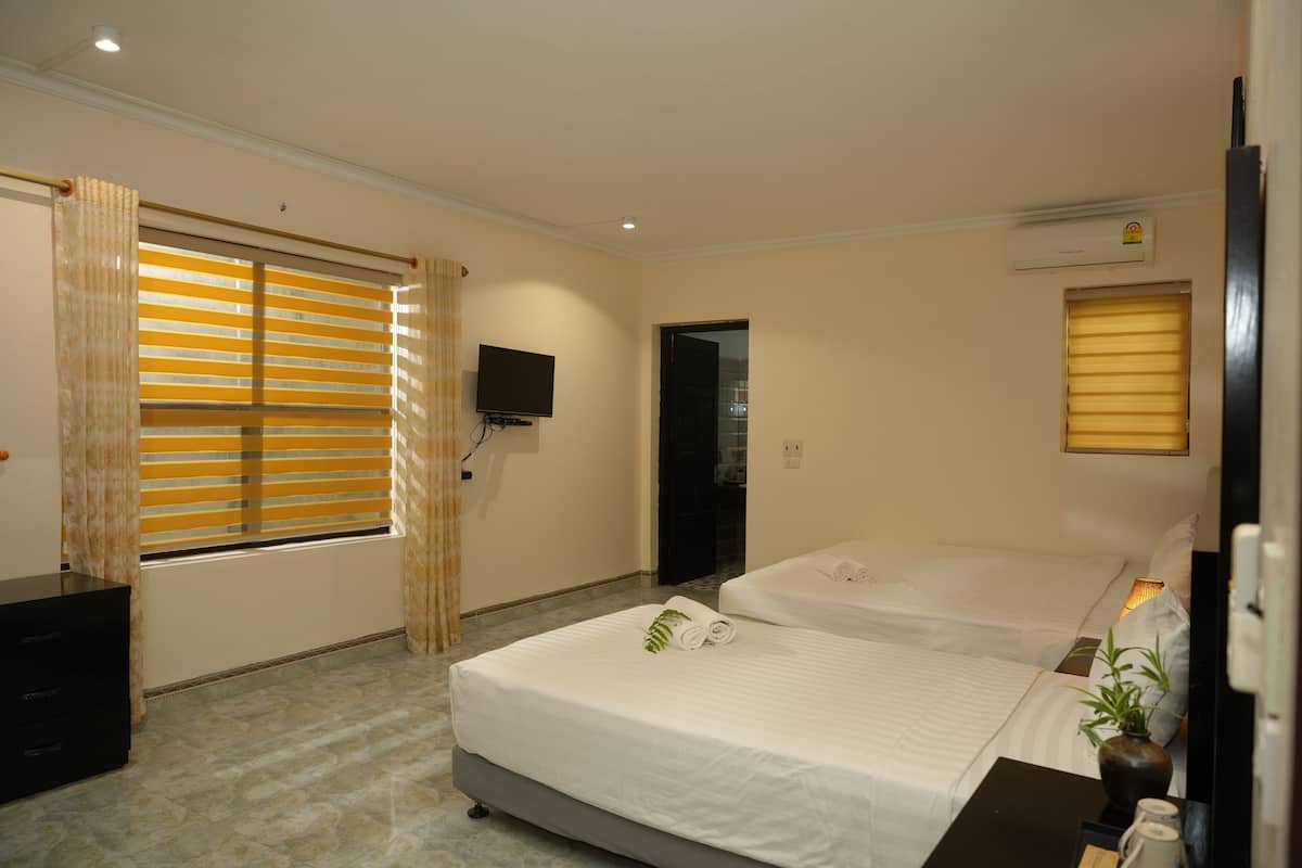 Habitación de hotel con dos camas, televisión, escritorio con lámpara y ventana con persianas.
