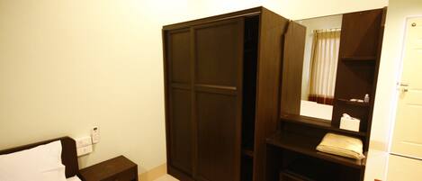 A hotel room with a bed, a wardrobe, a mirror, a small table, and a trash bin.