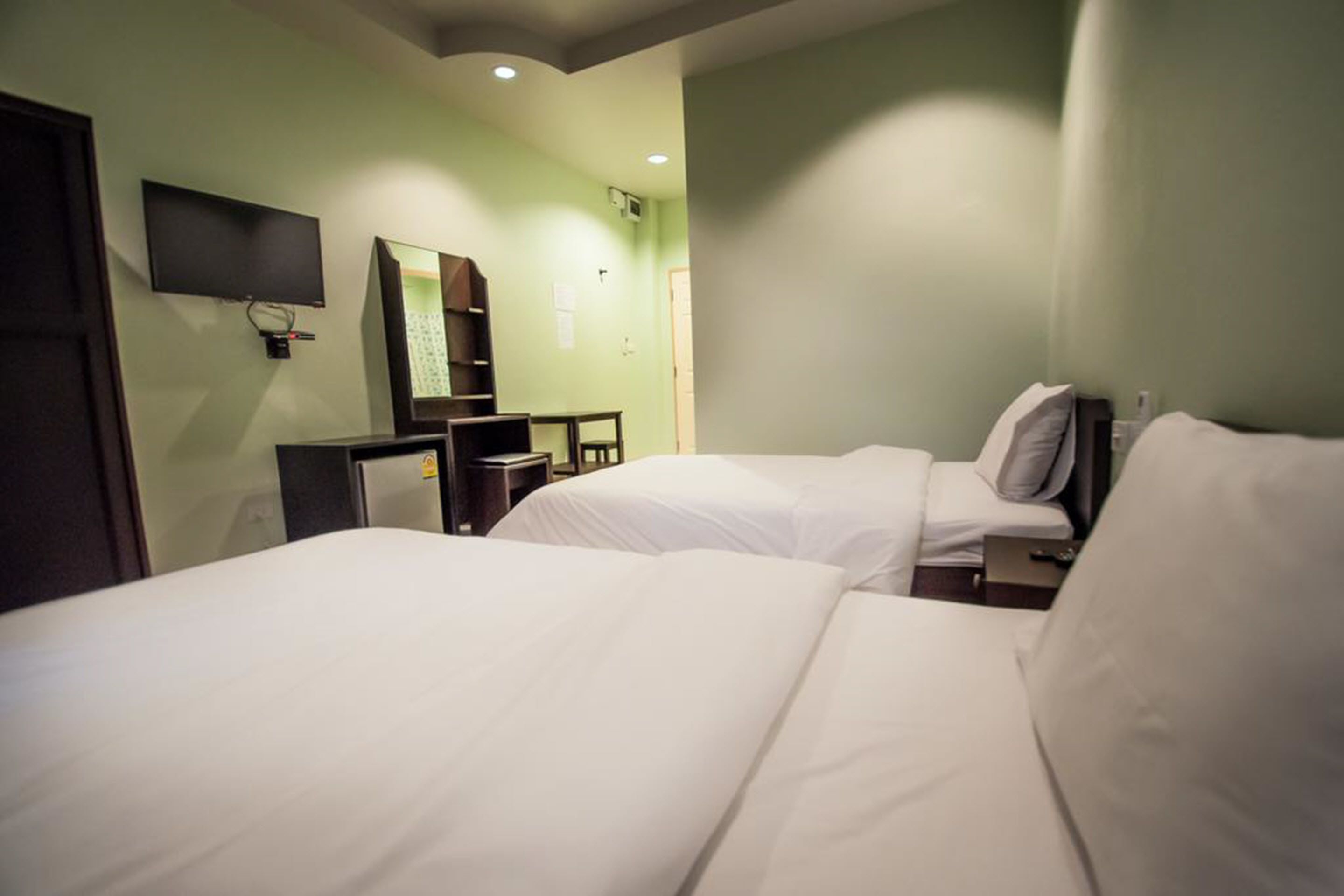 Habitación de hotel con dos camas, un escritorio, una silla, un televisor de pantalla plana montado en la pared y un espejo.