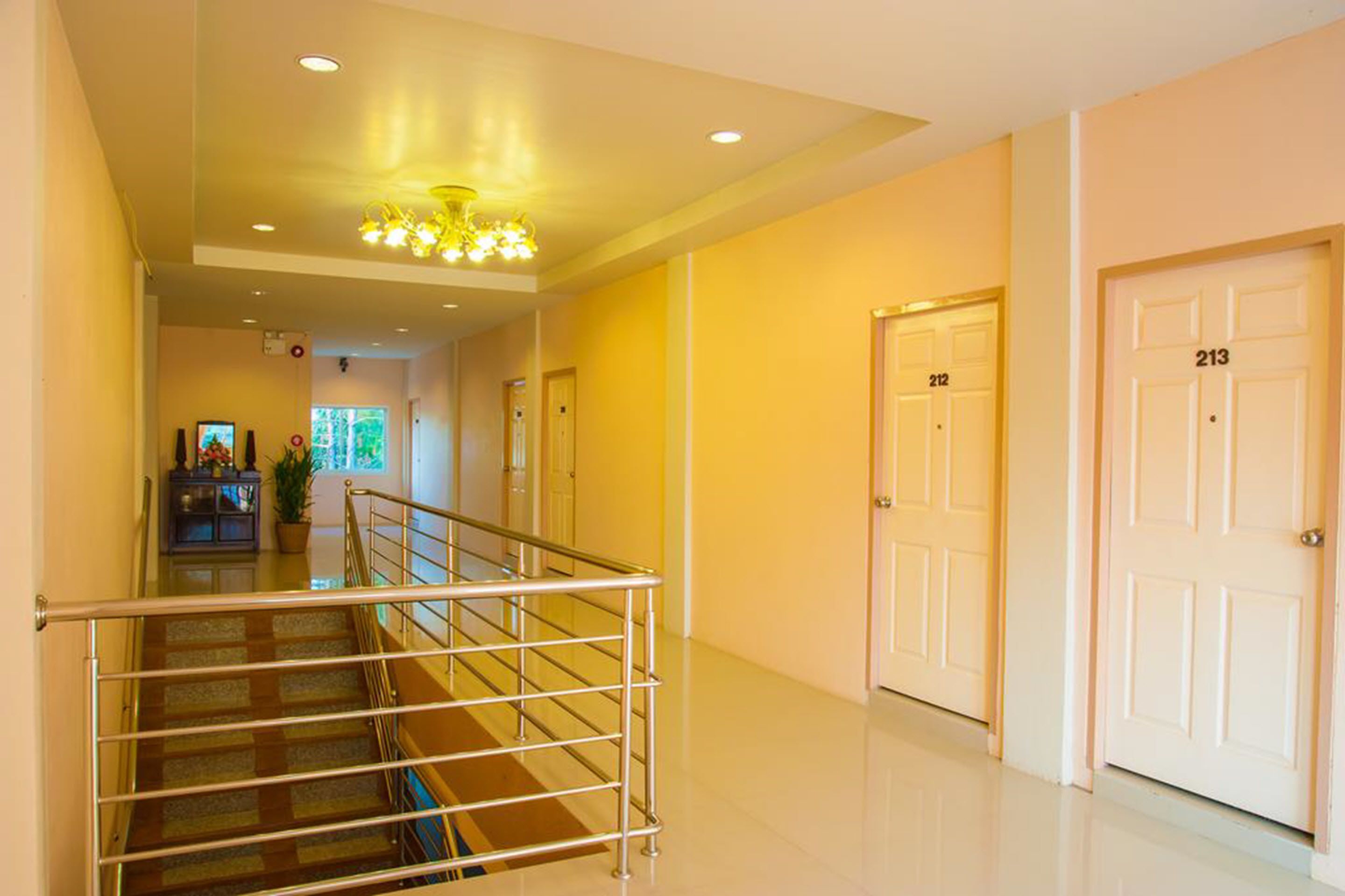 Un pasillo de hotel con una escalera, puertas numeradas 212 y 213, y un candelabro.