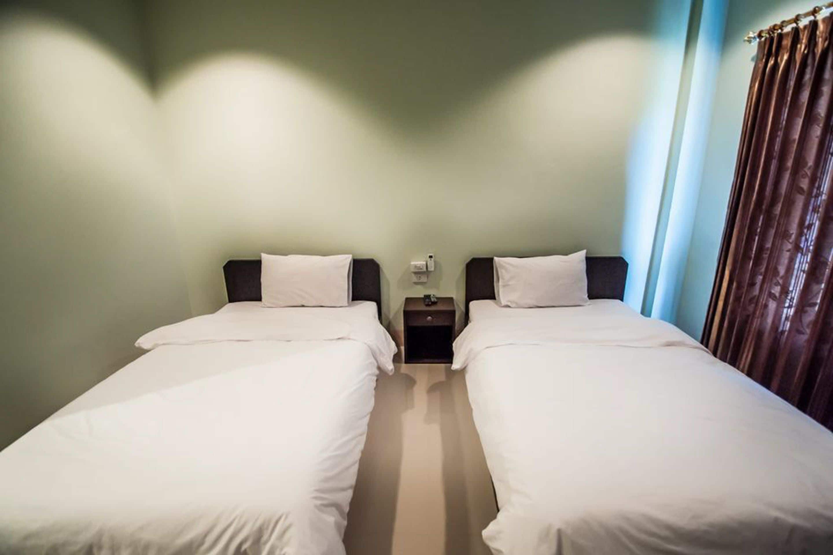 Habitación de hotel con dos camas individuales, una mesita de noche con lámpara y una ventana con cortinas.