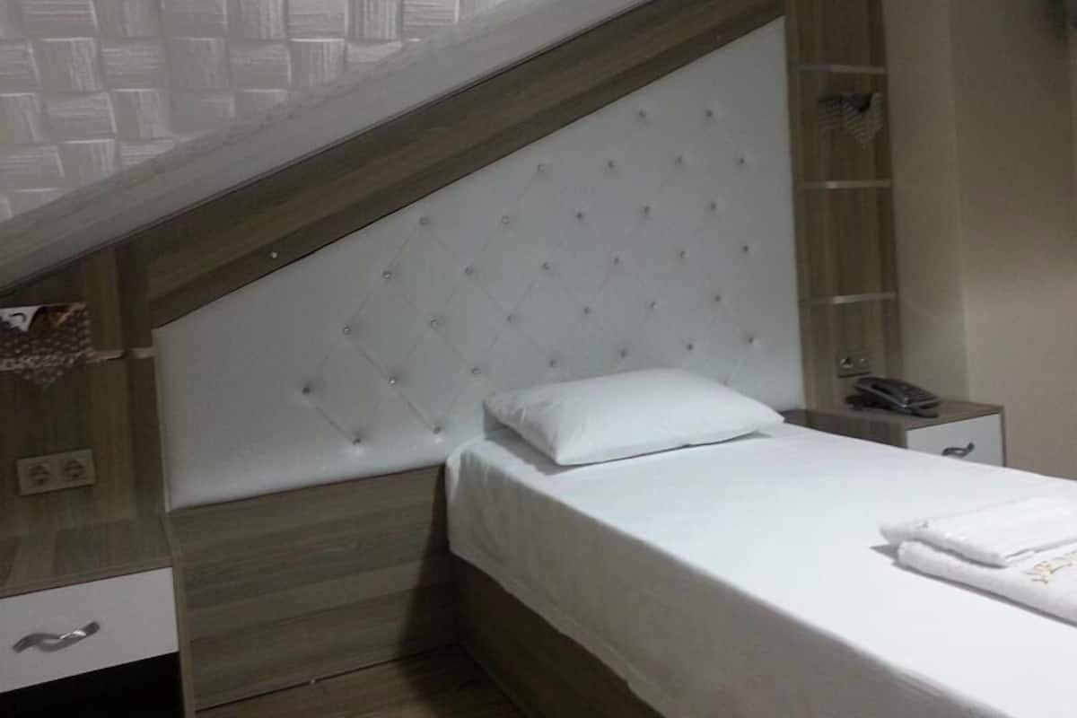 A bedroom with a bed, a nightstand, a telephone, and a shelf with a folded towel.