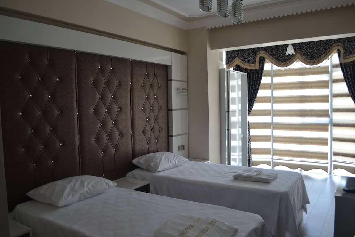 A hotel room with two beds, a large padded headboard, and a window with curtains.