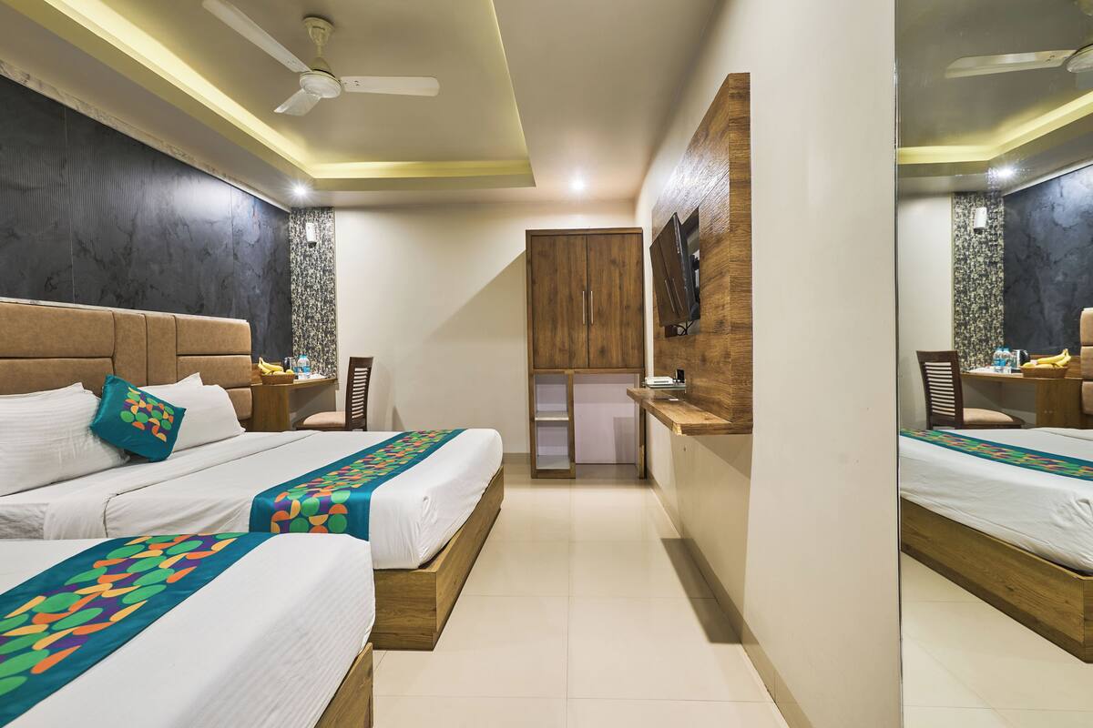 A hotel room with two beds, a wooden wardrobe, a desk, and a mirror.