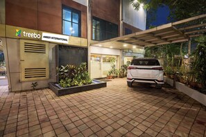 A building with a sign reading 'treebo AMBER INTERNATIONAL,' a white SUV parked in front, and potted plants around the entrance. - Treebo Amber International Mumbai Airport T2 (Mumbai)