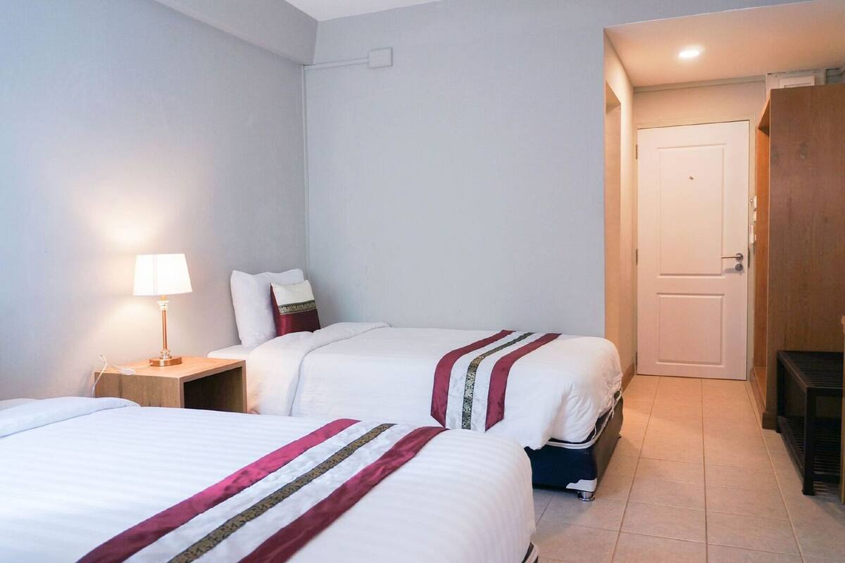 A hotel room with two beds, a nightstand with a lamp, a wardrobe, and a door.