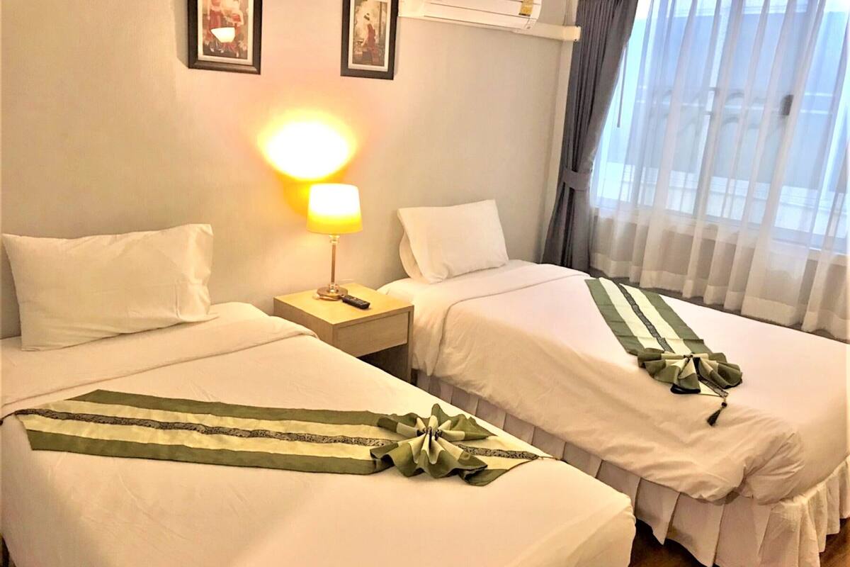 A hotel room with two beds, a nightstand with a lamp, and a window with curtains.