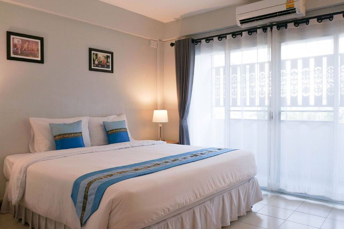 A hotel room with a large bed, a nightstand, a lamp, and a window with curtains.