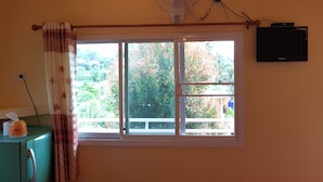 A room with a window, a standing fan, a small heater, and a television mounted on the wall. - Ban Mae Resort (Khao Kho)