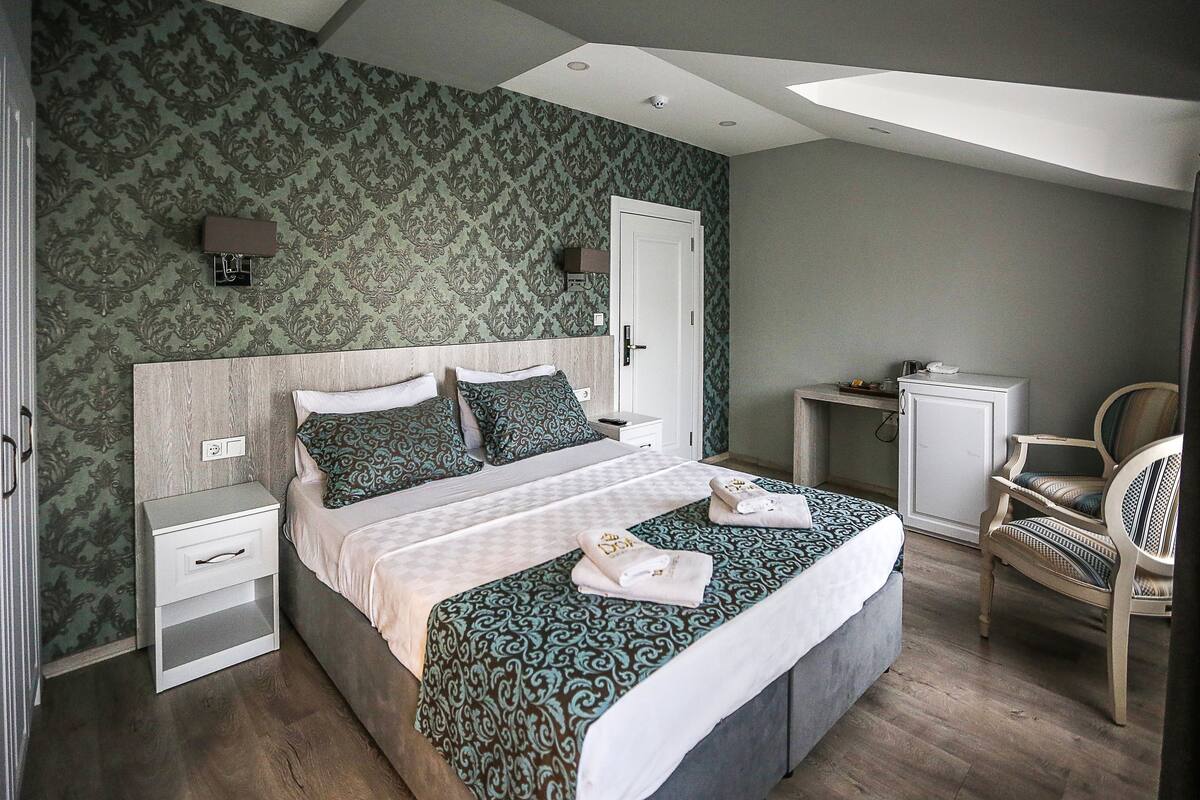 A bedroom with a large bed, a nightstand, a chair, and a desk.