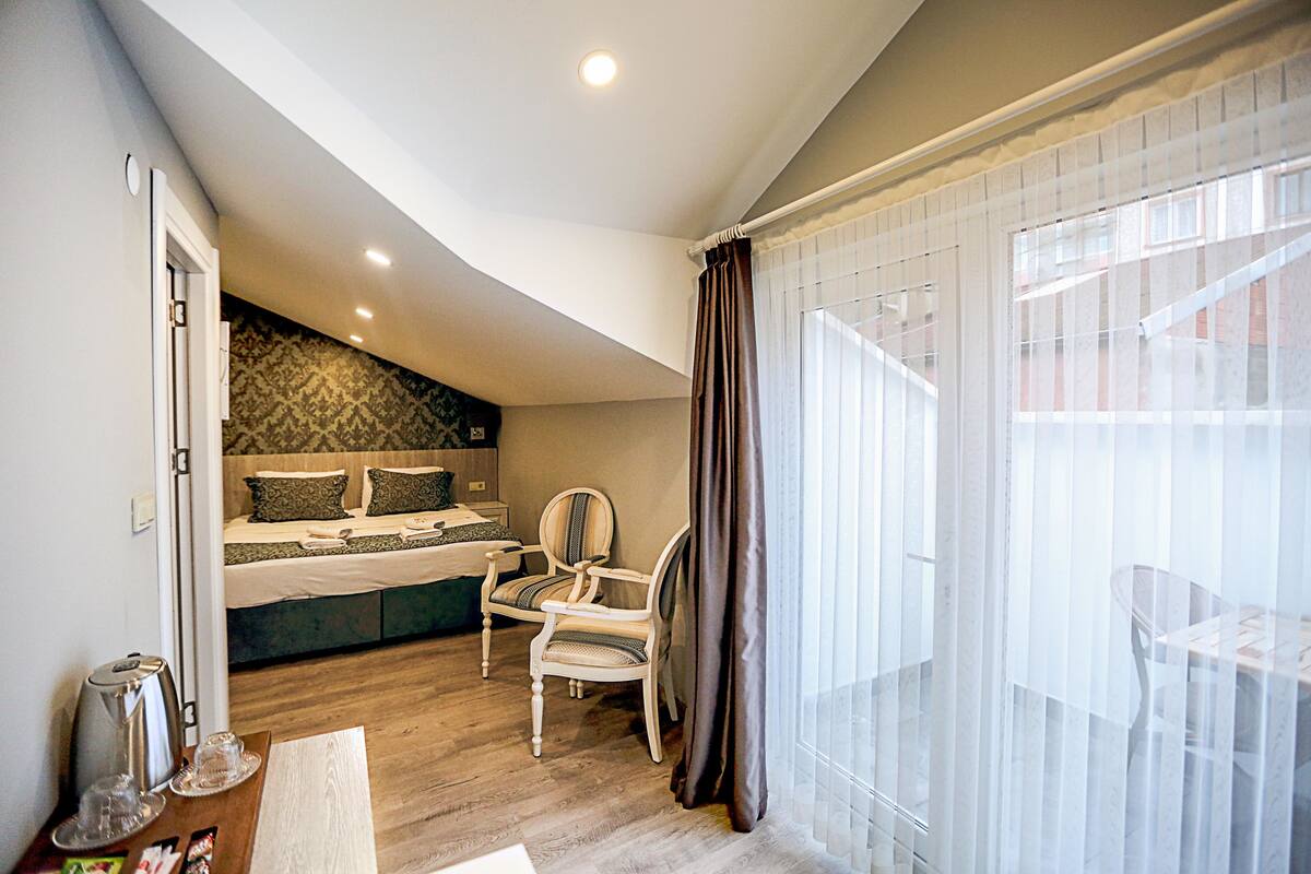 A bedroom with a bed, two chairs, a table, and a window with curtains.