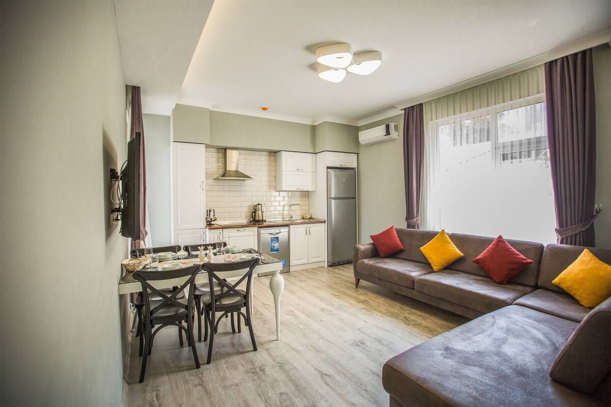 A compact living space with a dining area, kitchenette, and a sofa with colorful cushions.