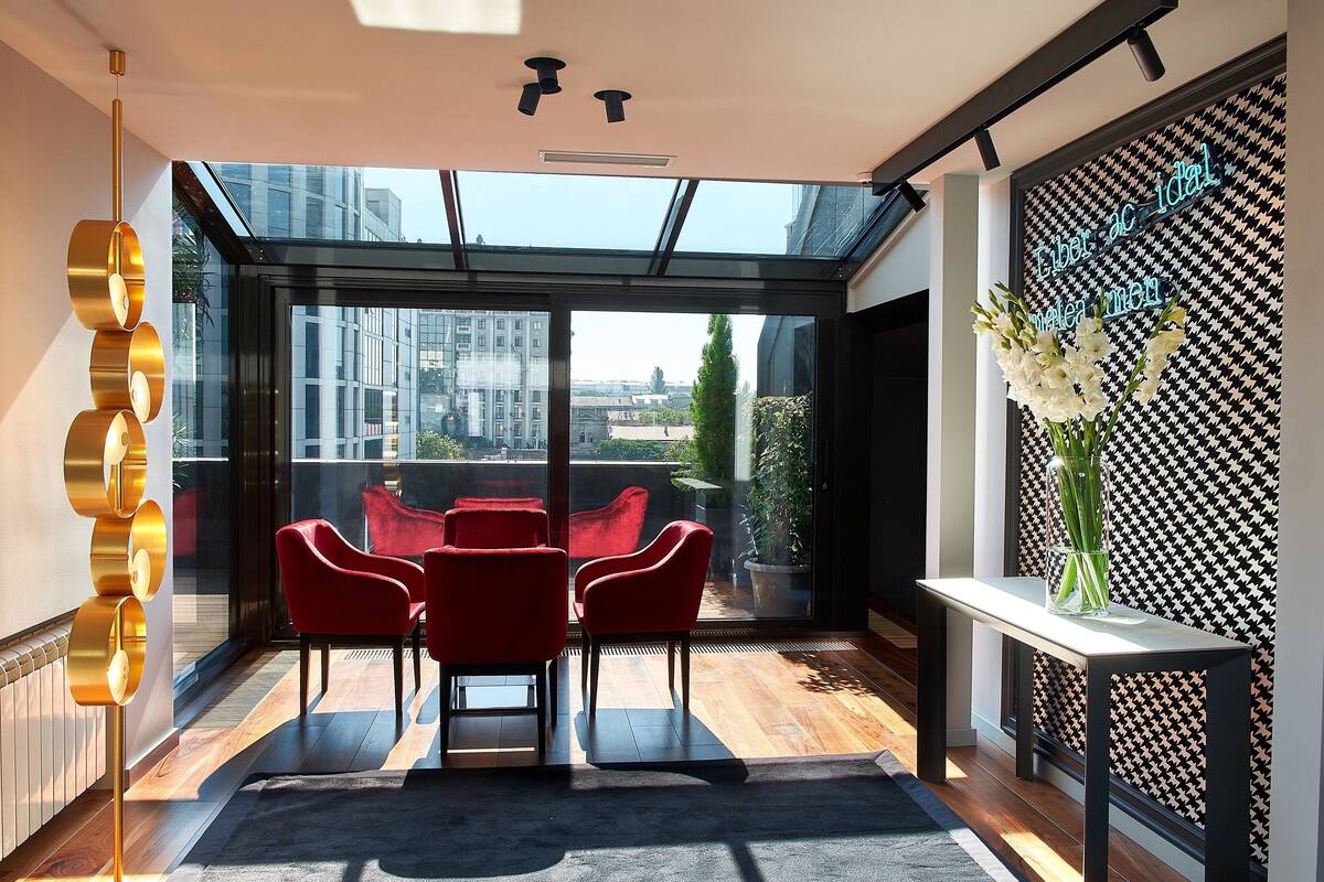 A modern interior with a glass ceiling, red chairs, a white table, and a potted plant.