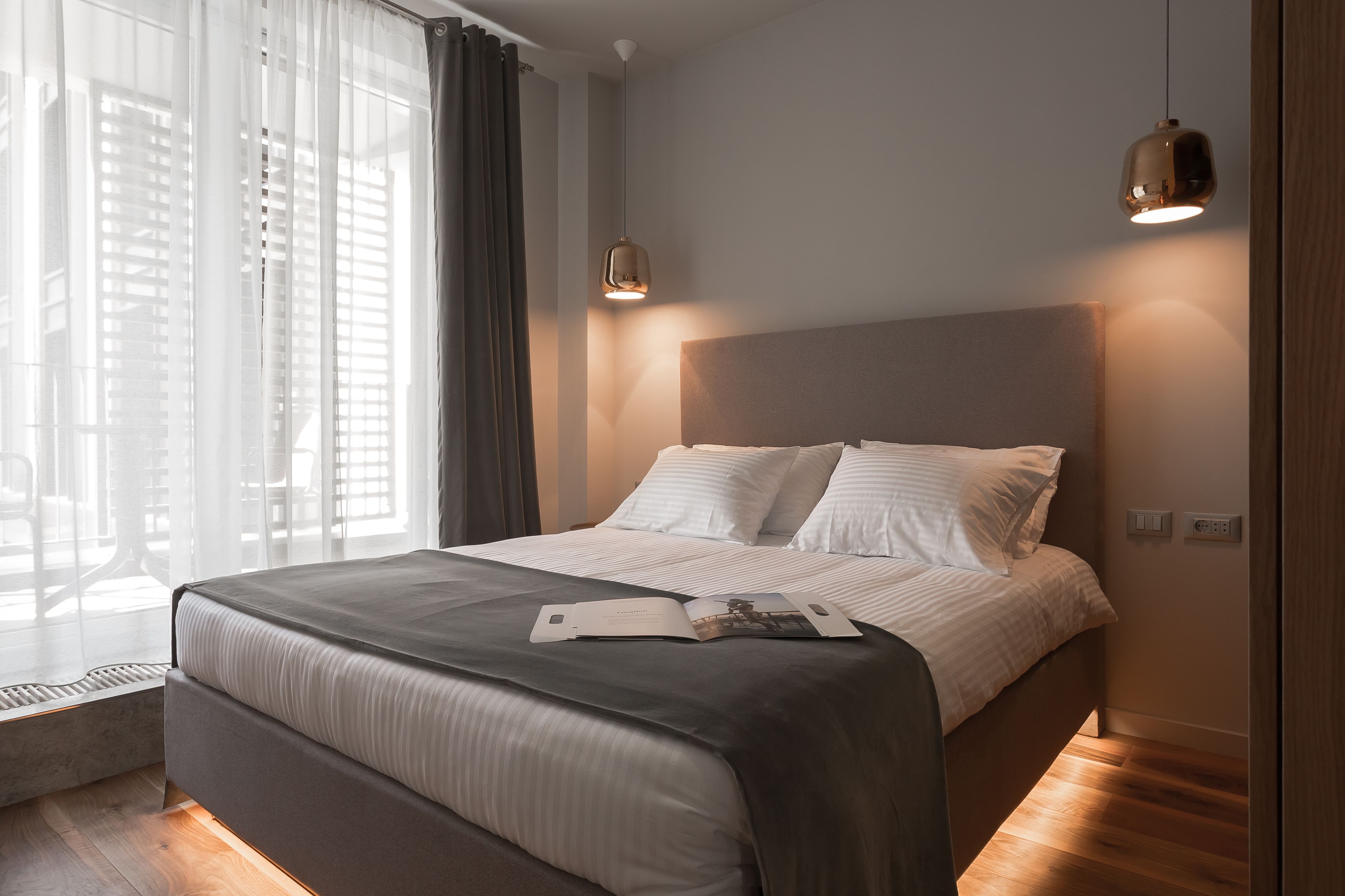 Ett modernt hotellrum med en stor säng, ett nattduksbord och ett fönster med gardiner.