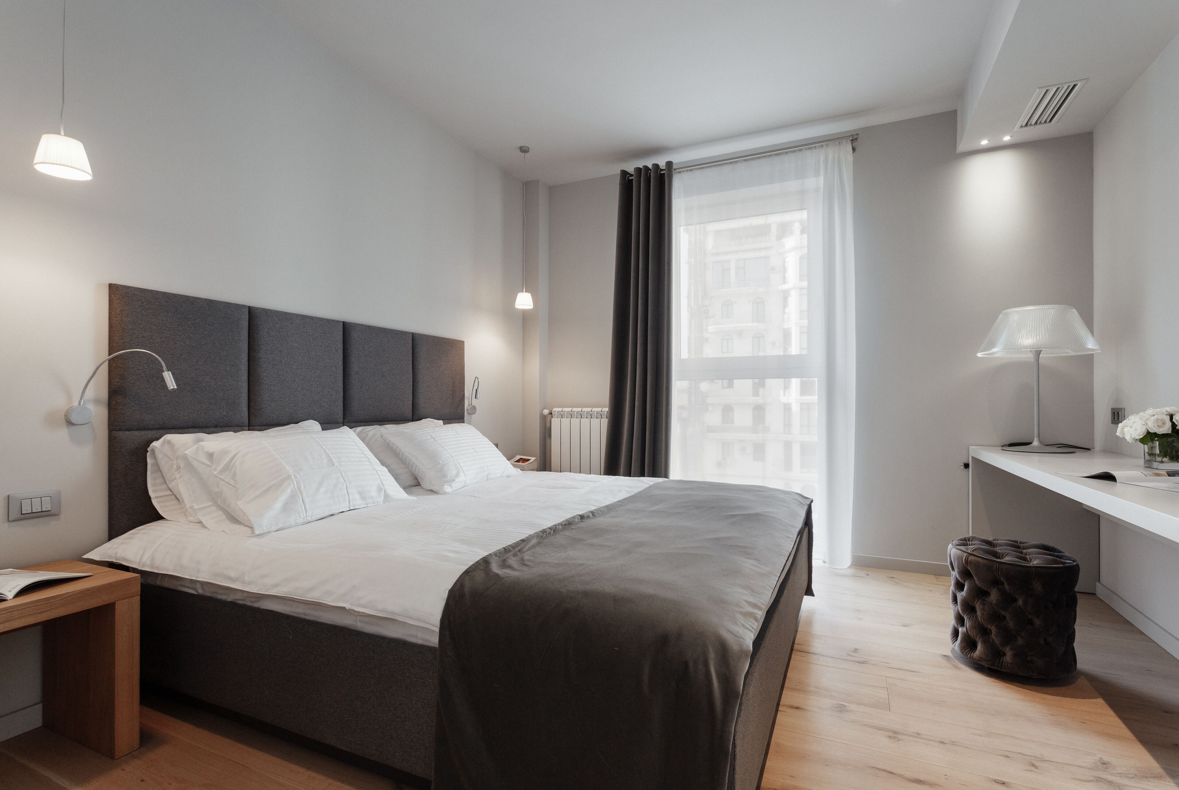 Un dormitorio moderno con una cama grande, mesitas de noche, un escritorio y una ventana con cortinas.