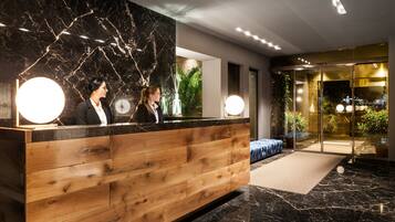 A reception area with a wooden counter, marble wall, and glass doors leading to a garden.