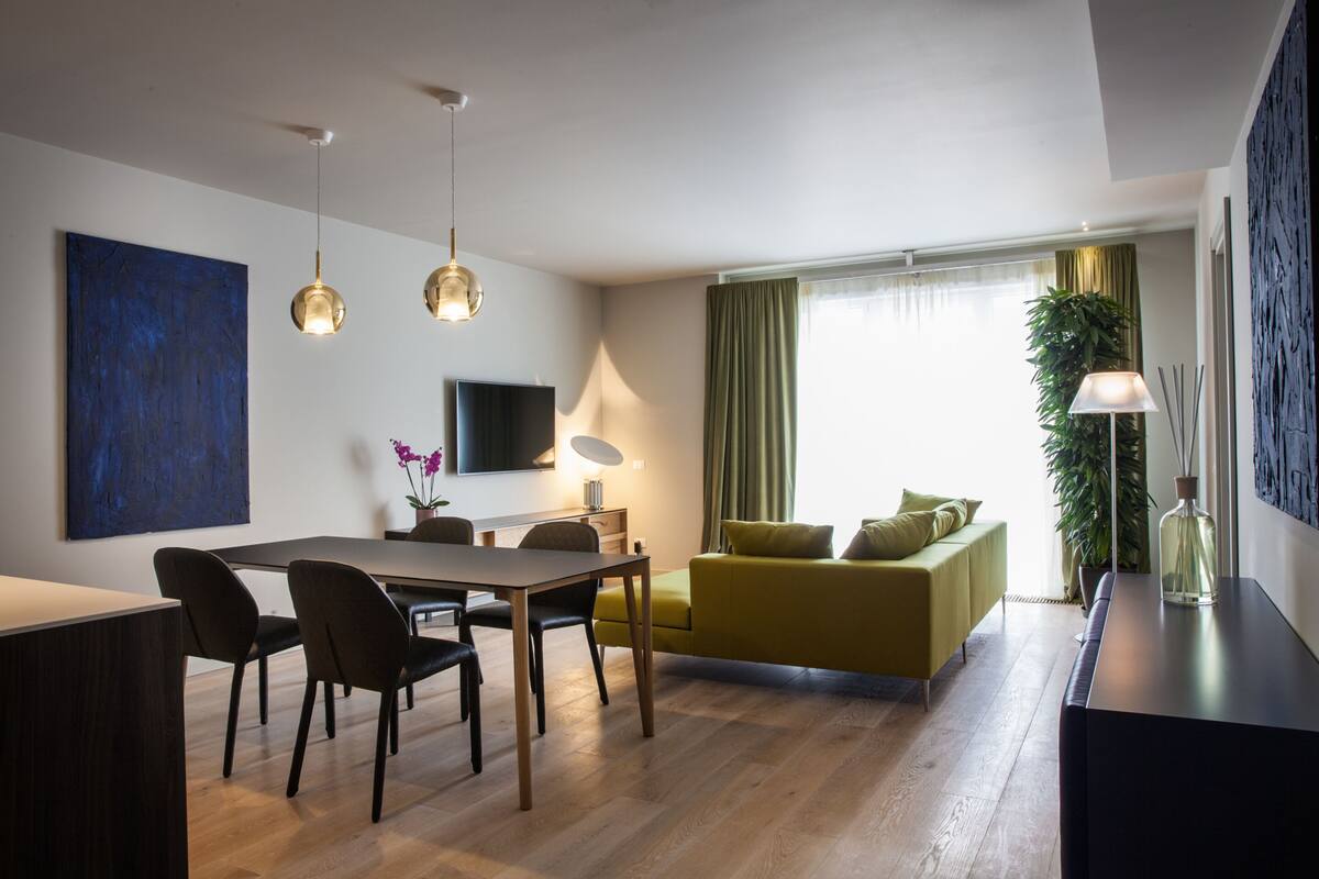 A modern living room with a dining area, a sofa, and a TV mounted on the wall.