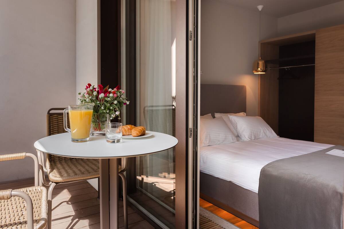 A hotel room with a bed, a small table with breakfast items, and a view of the outside.