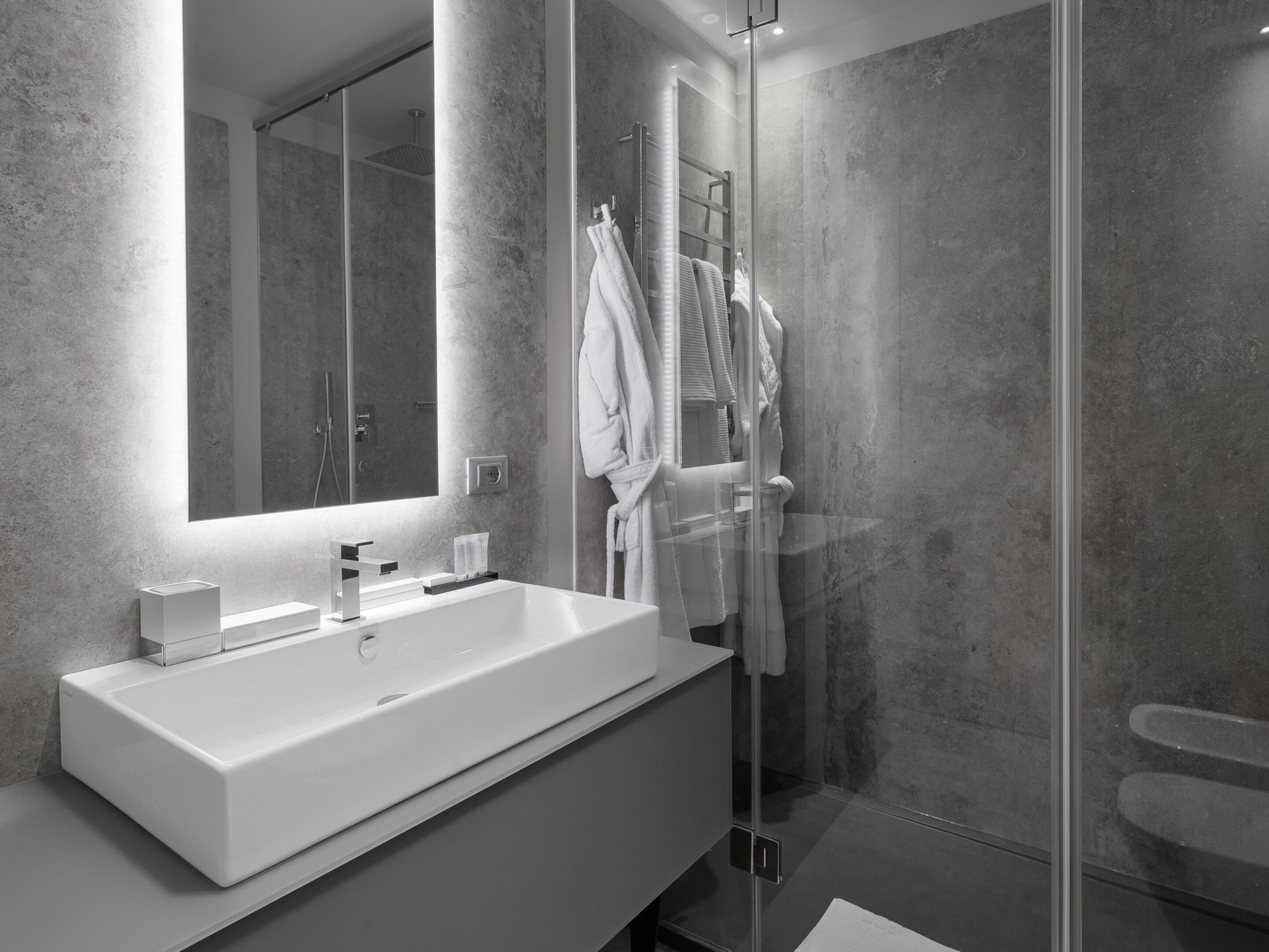 Une salle de bain moderne avec un grand lavabo blanc, une cabine de douche en verre et un miroir au-dessus du lavabo.