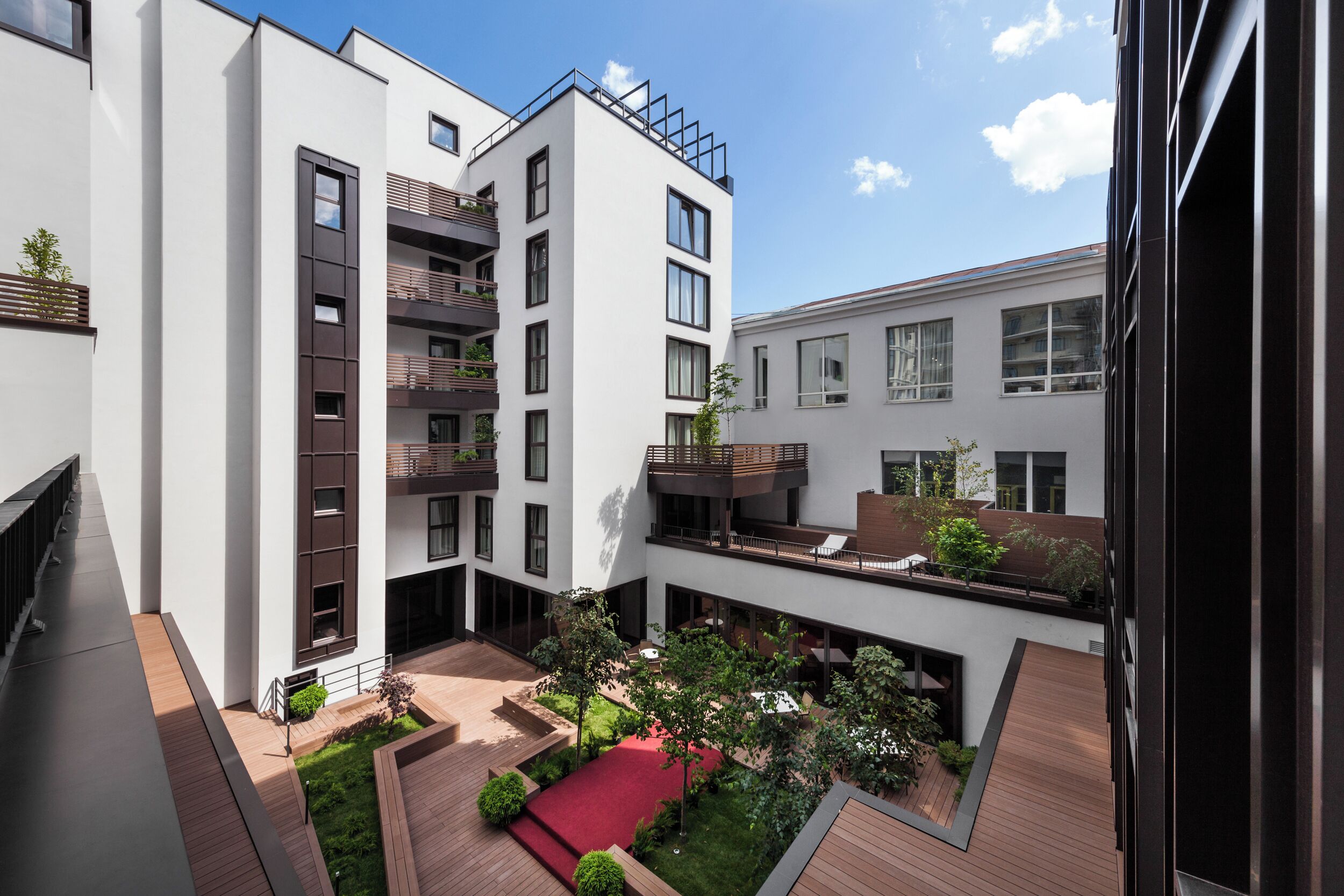 A modern apartment complex with multiple balconies, a courtyard with greenery, and a red carpet.
