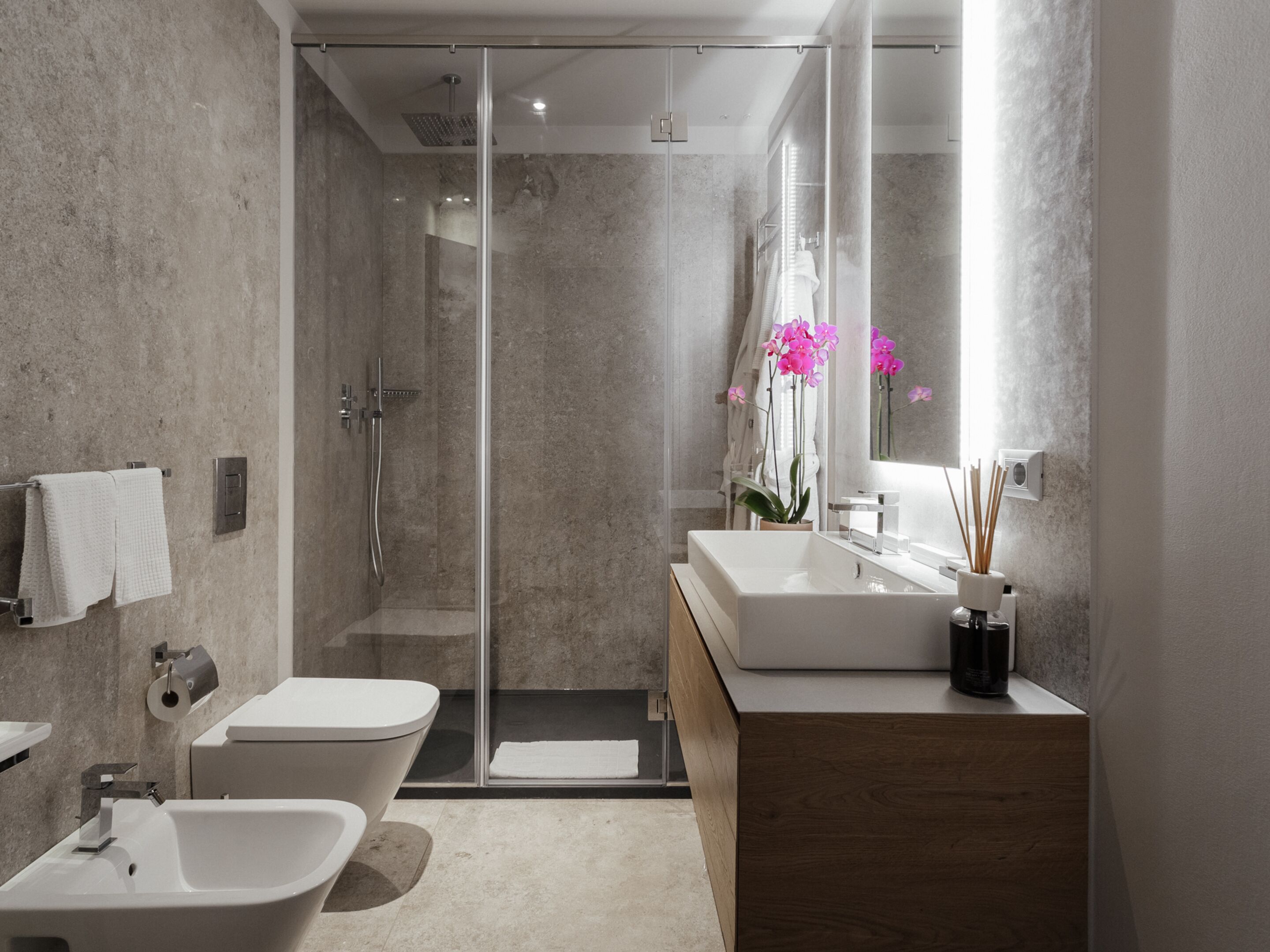 A modern bathroom with a glass-enclosed shower, a freestanding bathtub, a vanity with a mirror, and a toilet.