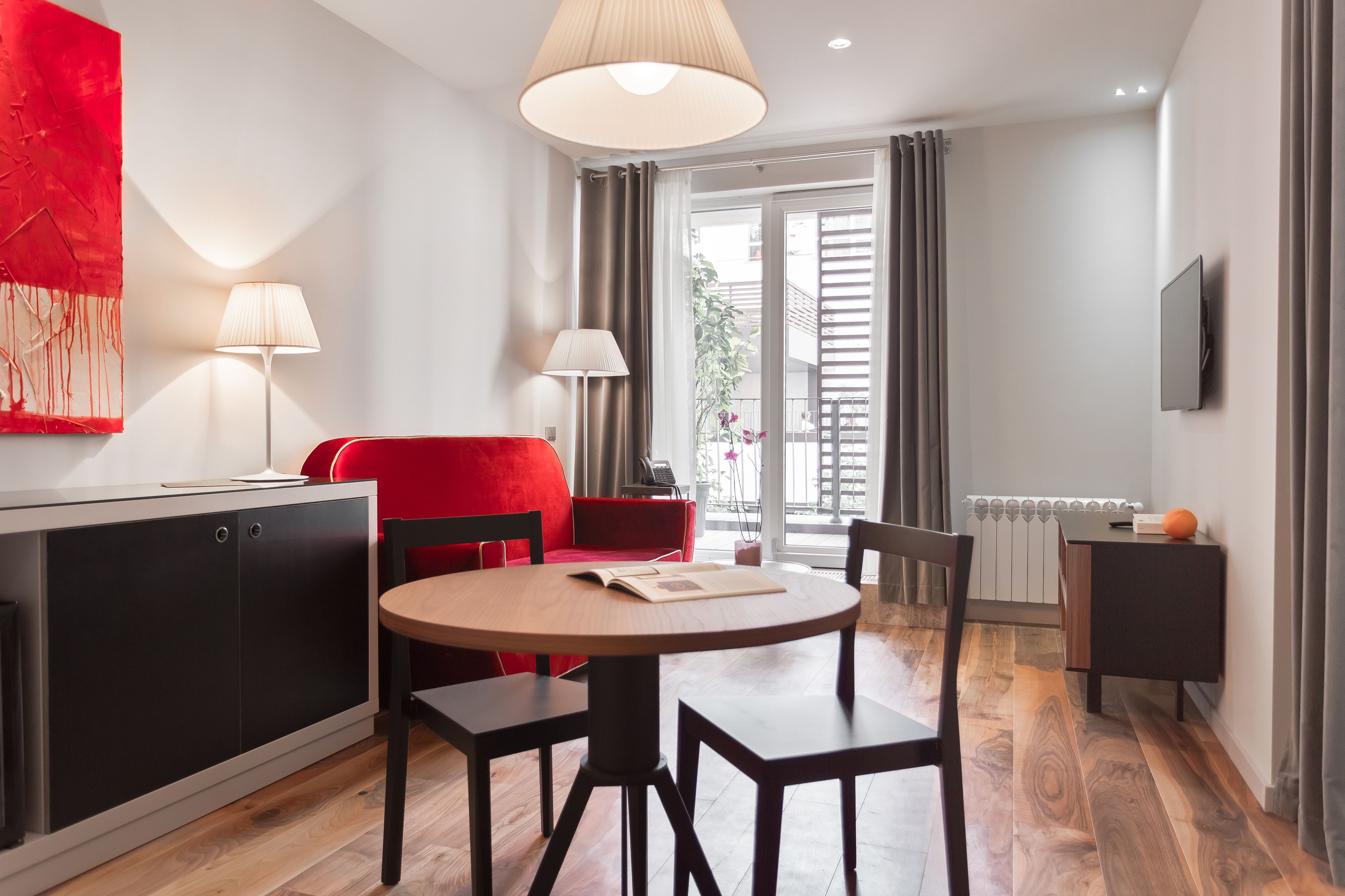 A modern living room with a red sofa, a round wooden table, and a TV mounted on the wall.
