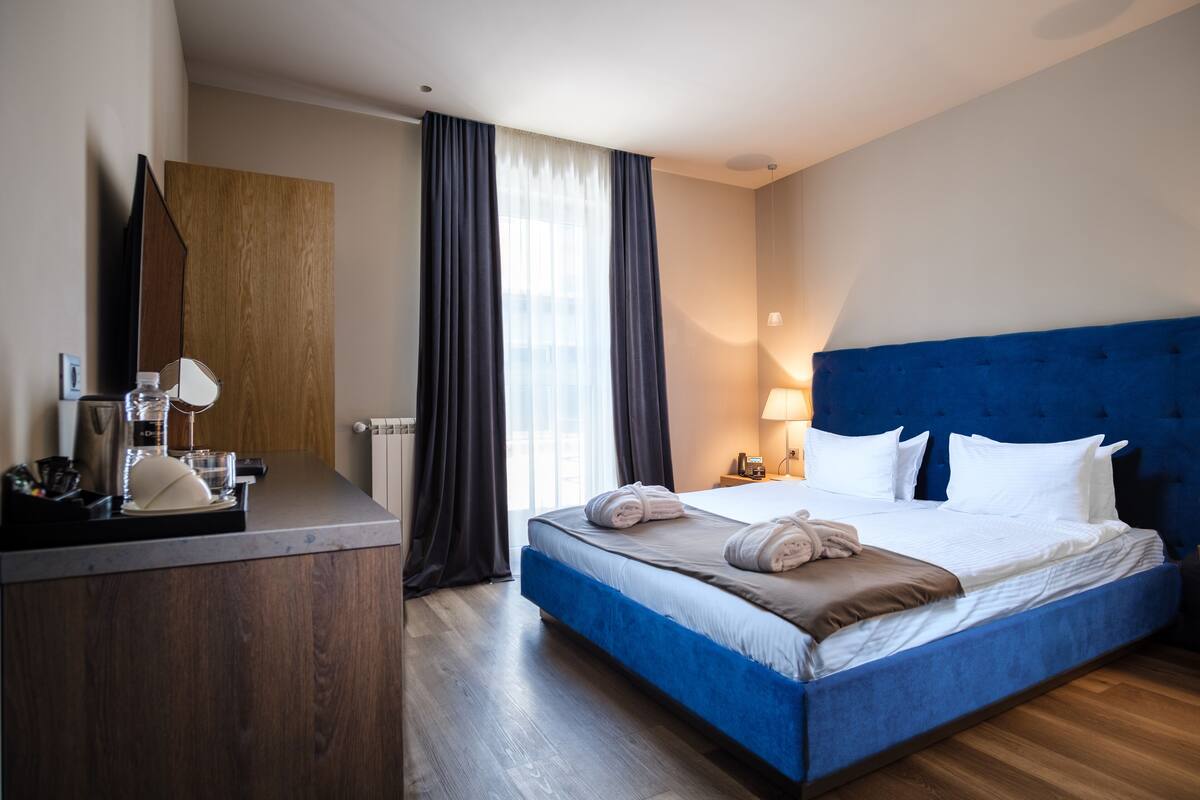 A hotel room with a large bed, a desk with a mirror, a lamp, and a window with curtains.