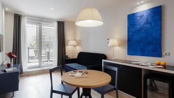 Una habitación de hotel moderna con comedor, sofá, mesa redonda y un cuadro azul grande en la pared.