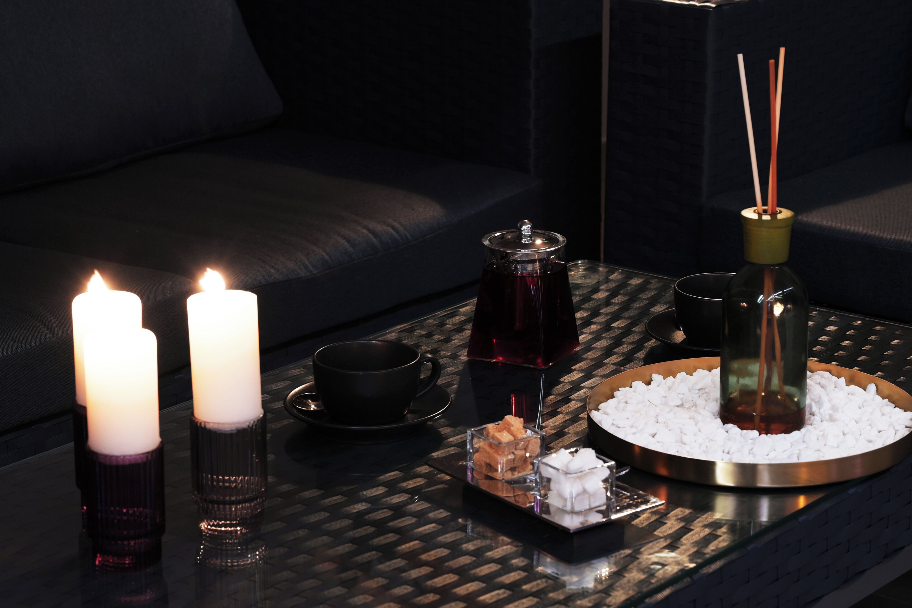 A tray with candles, a teapot, a cup, and a diffuser on a textured table.