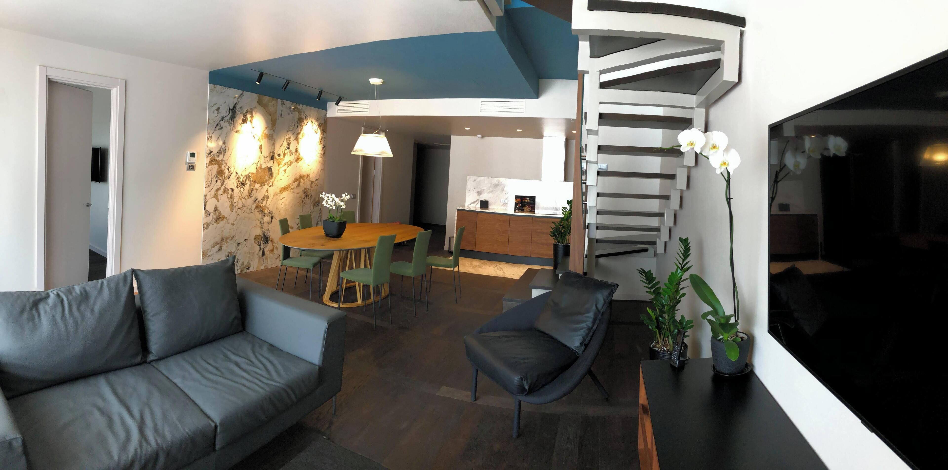 Una sala de estar moderna con un sofá, una mesa de comedor con sillas, una escalera y una zona de cocina.