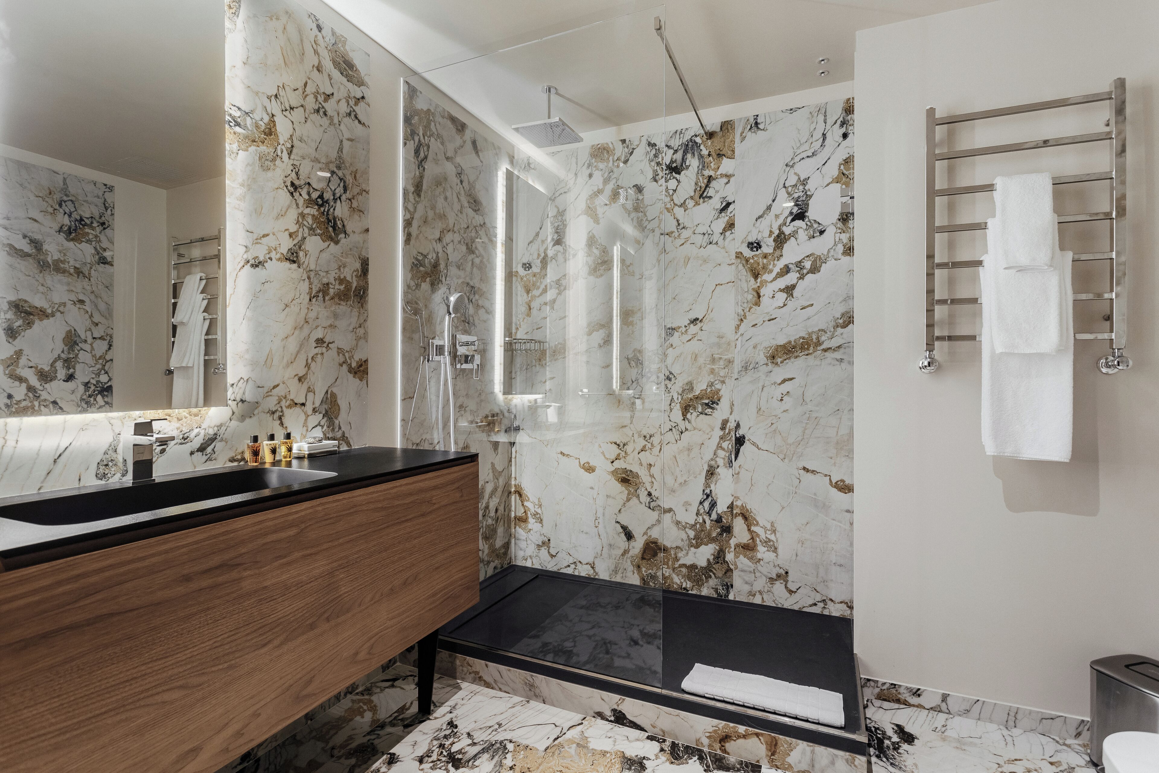 A modern bathroom with a marble backsplash, a wooden vanity, a black sink, and a glass shower enclosure.