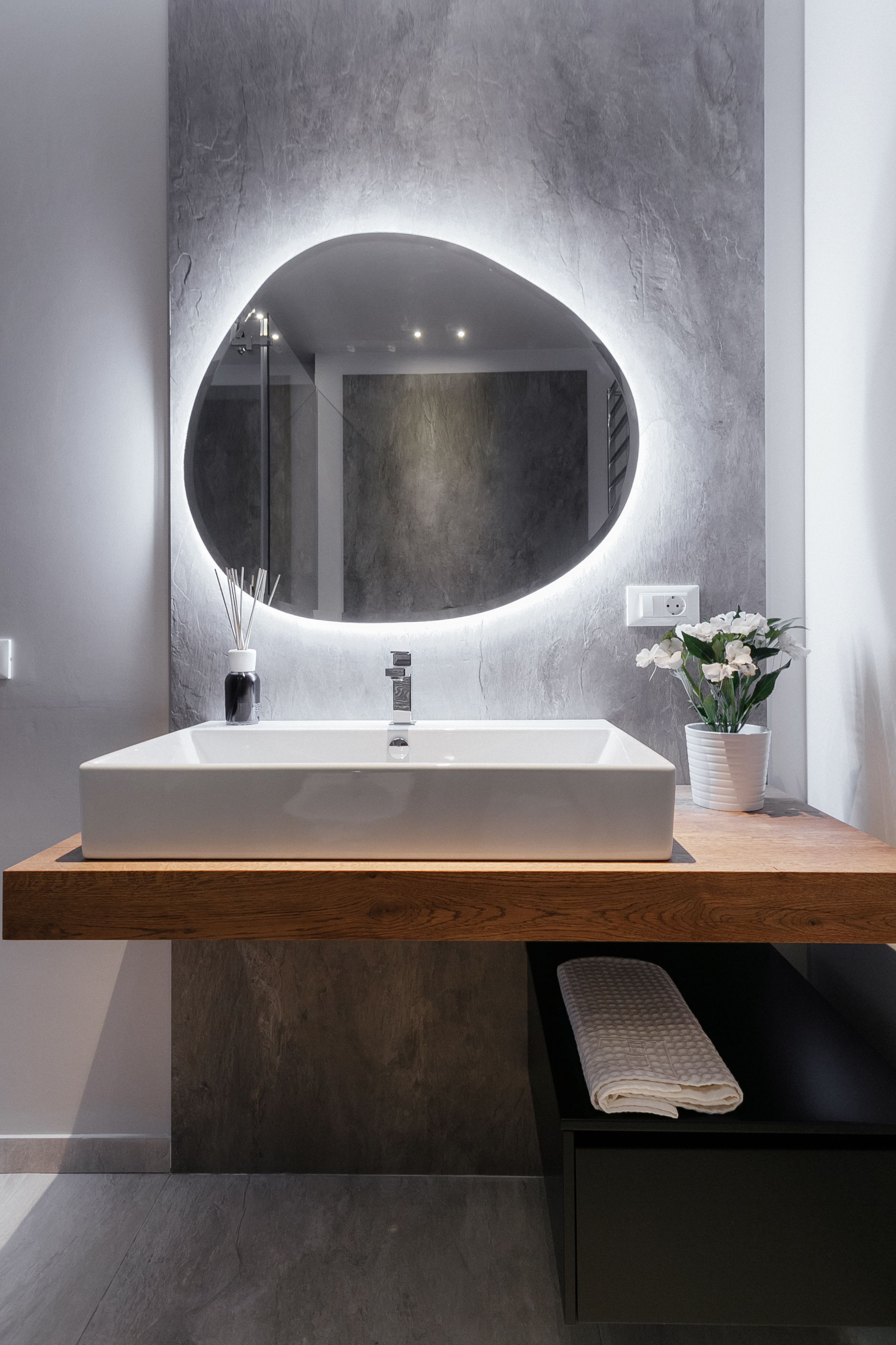 Ein modernes Badezimmer mit einem rechteckigen Waschbecken, einem großen, ovalen Spiegel und einer Topfpflanze.