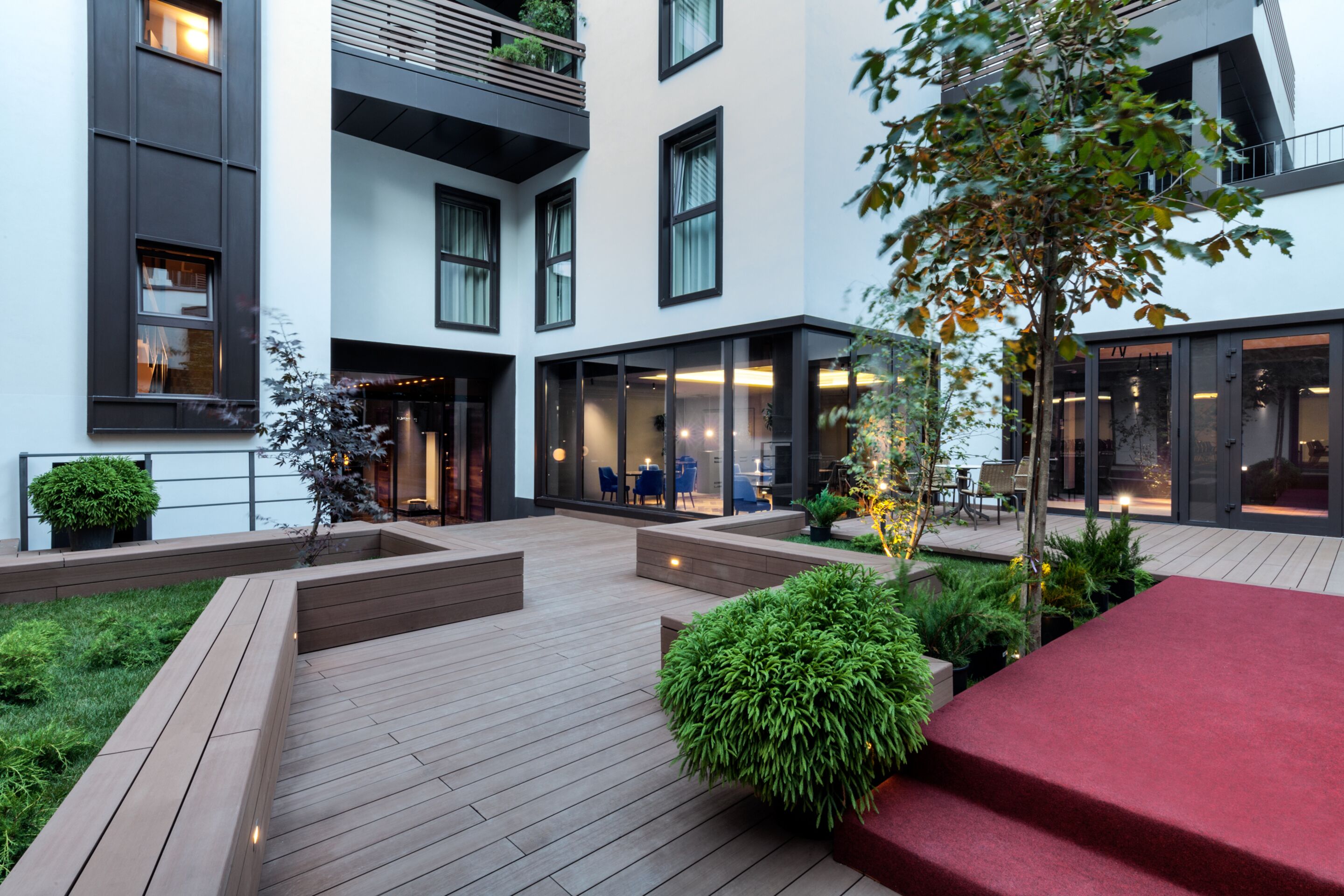 Un bâtiment moderne doté d’une cour intérieure aménagée avec une terrasse en bois, des jardinières et des espaces de détente.