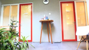 A room with two red-framed doors, a small wooden table with items on it, and a potted plant. - Buton Backpaker Lodge - Hostel (Bandung)