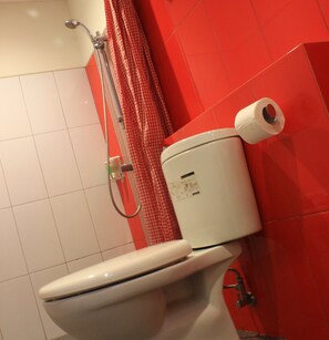 A toilet with a white tank and lid, a red shower curtain, and a white tiled floor.