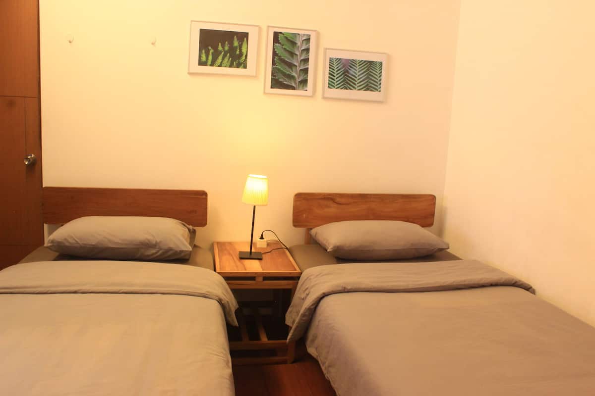 Una habitación con dos camas individuales, una mesita de noche con lámpara y tres láminas enmarcadas con motivos botánicos en la pared.
