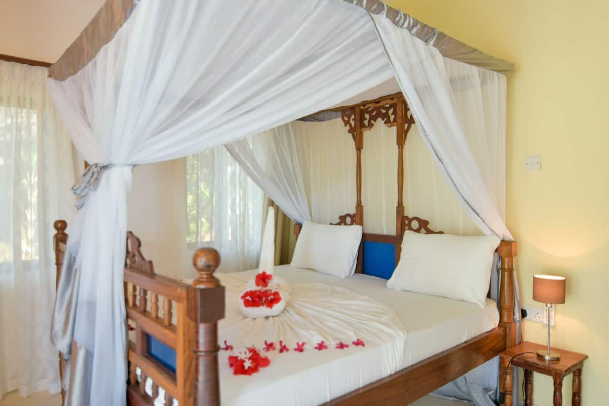 A four-poster canopy bed with white bedding and a floral arrangement.