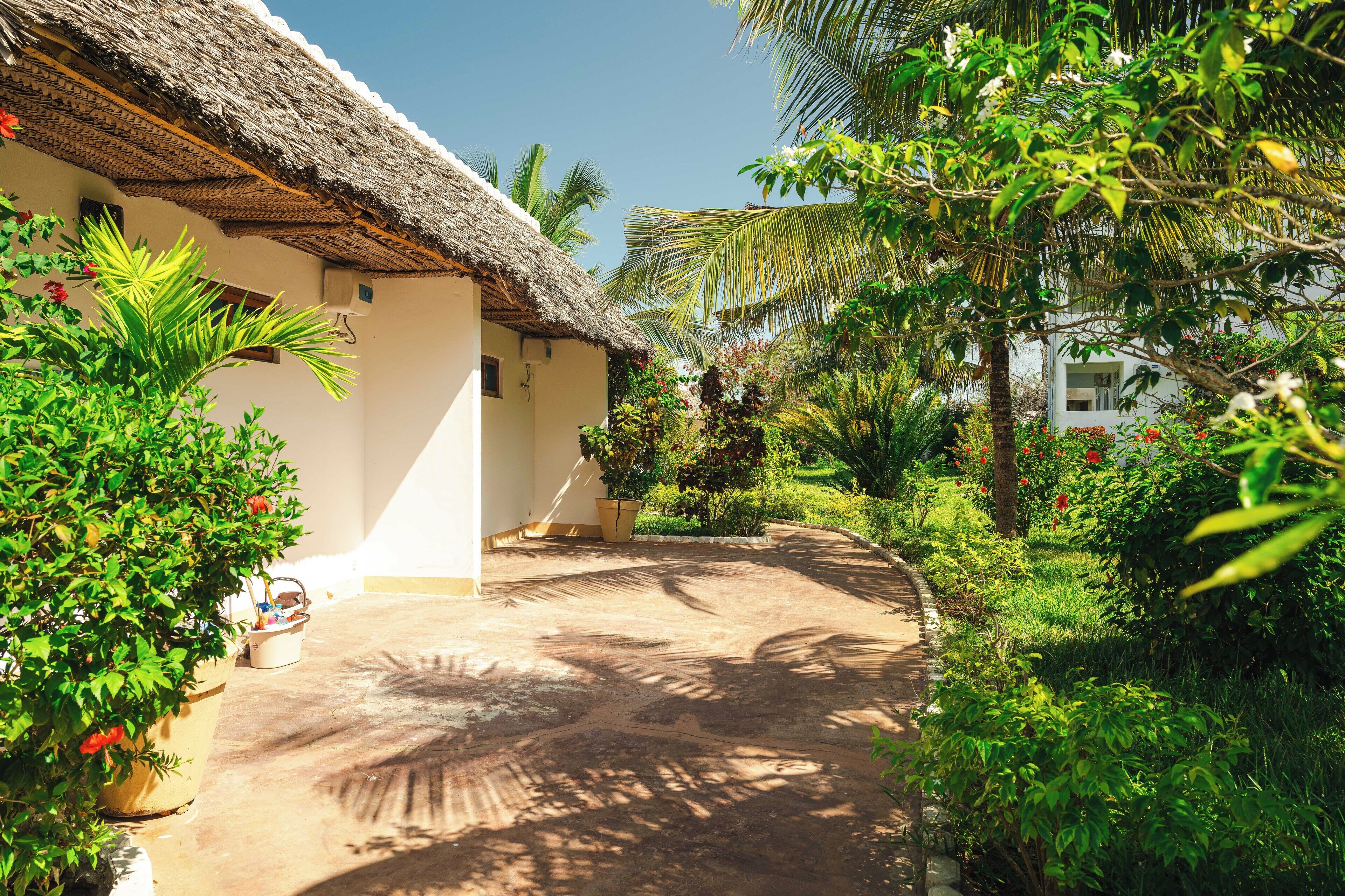 A thatched-roof building surrounded by lush greenery and a well-maintained garden path.