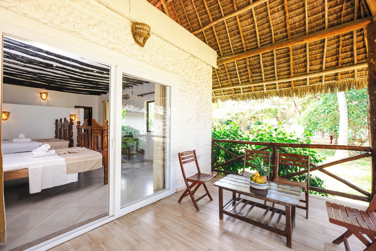 A room with a bed, a table with fruit, and a balcony with a view of greenery.
