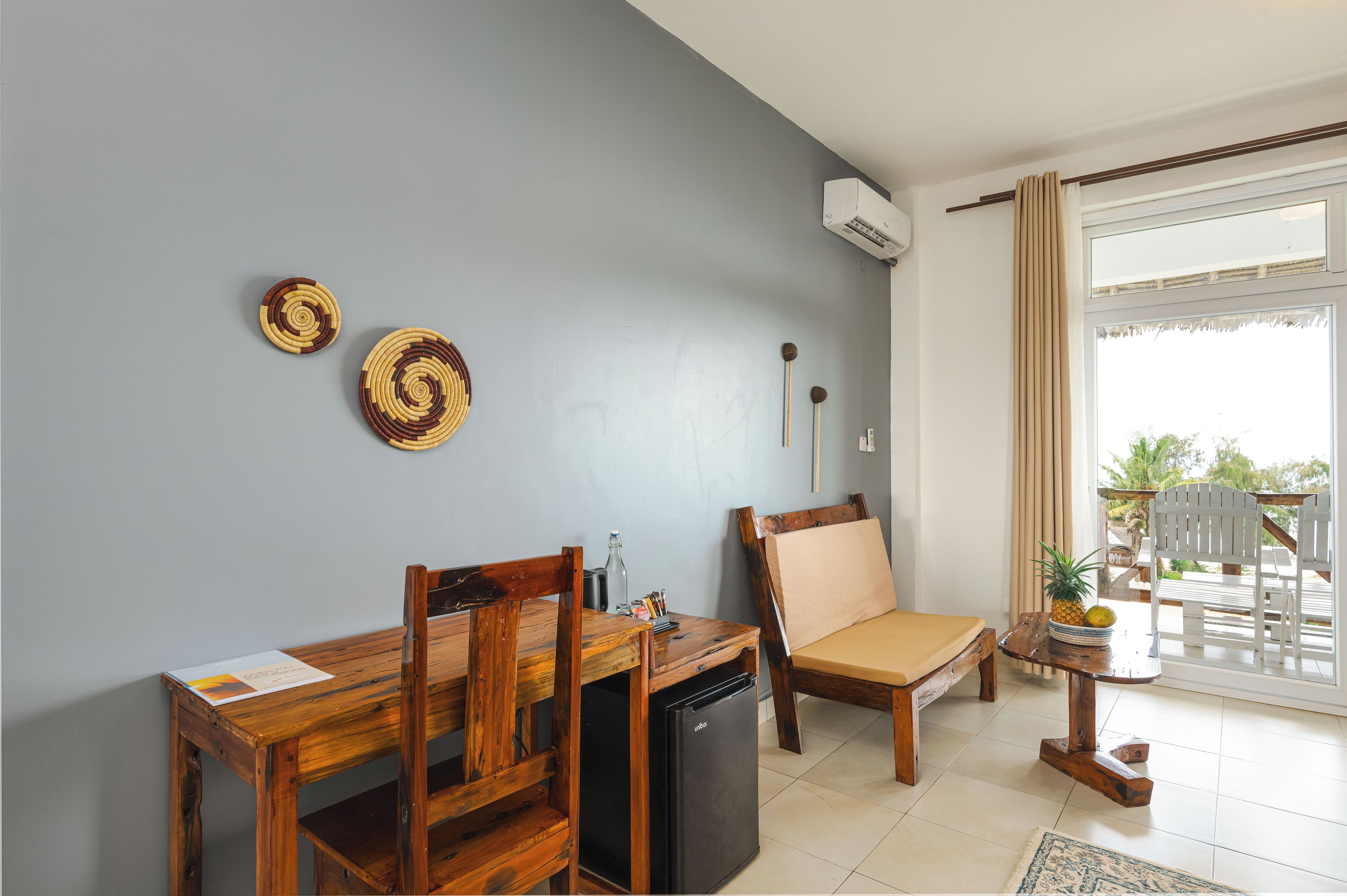 A room with a dining table, chairs, a small refrigerator, a sofa, and a window with curtains.