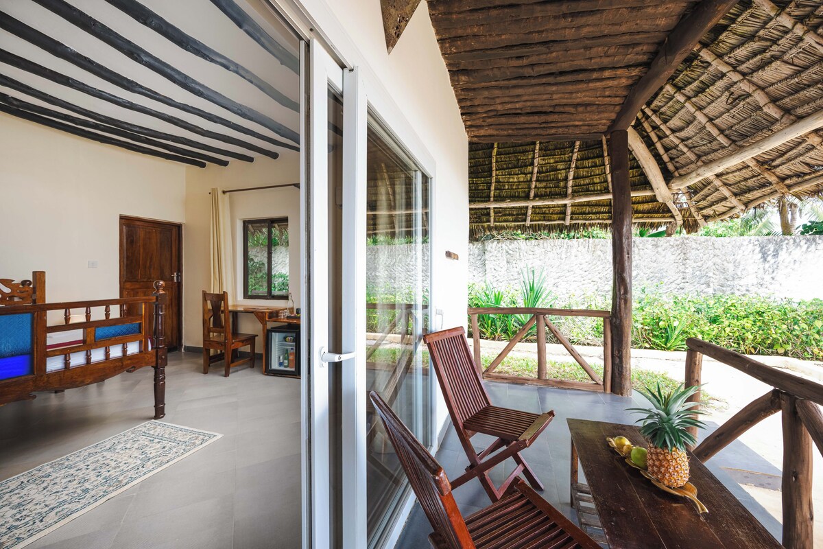 A room with a wooden ceiling, a glass door leading outside, a wooden table with a pineapple, and a chair.