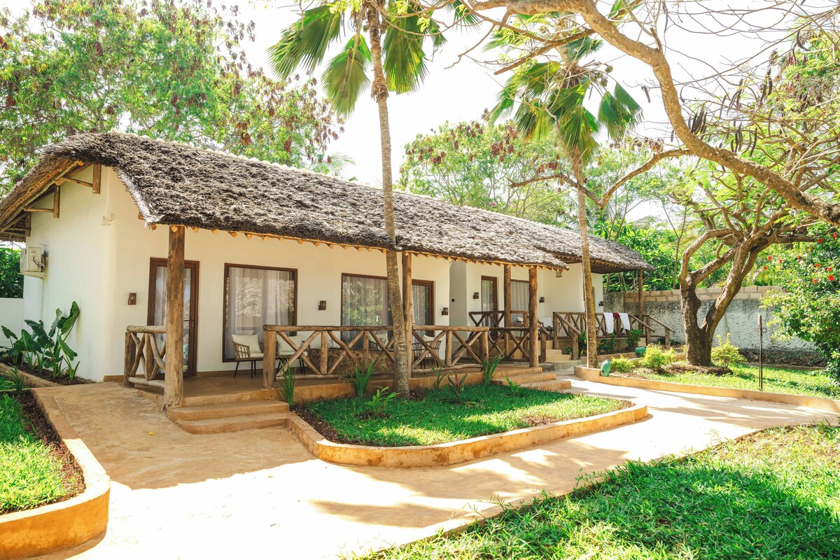 A single-story building with a thatched roof, a covered porch, and a small garden area.