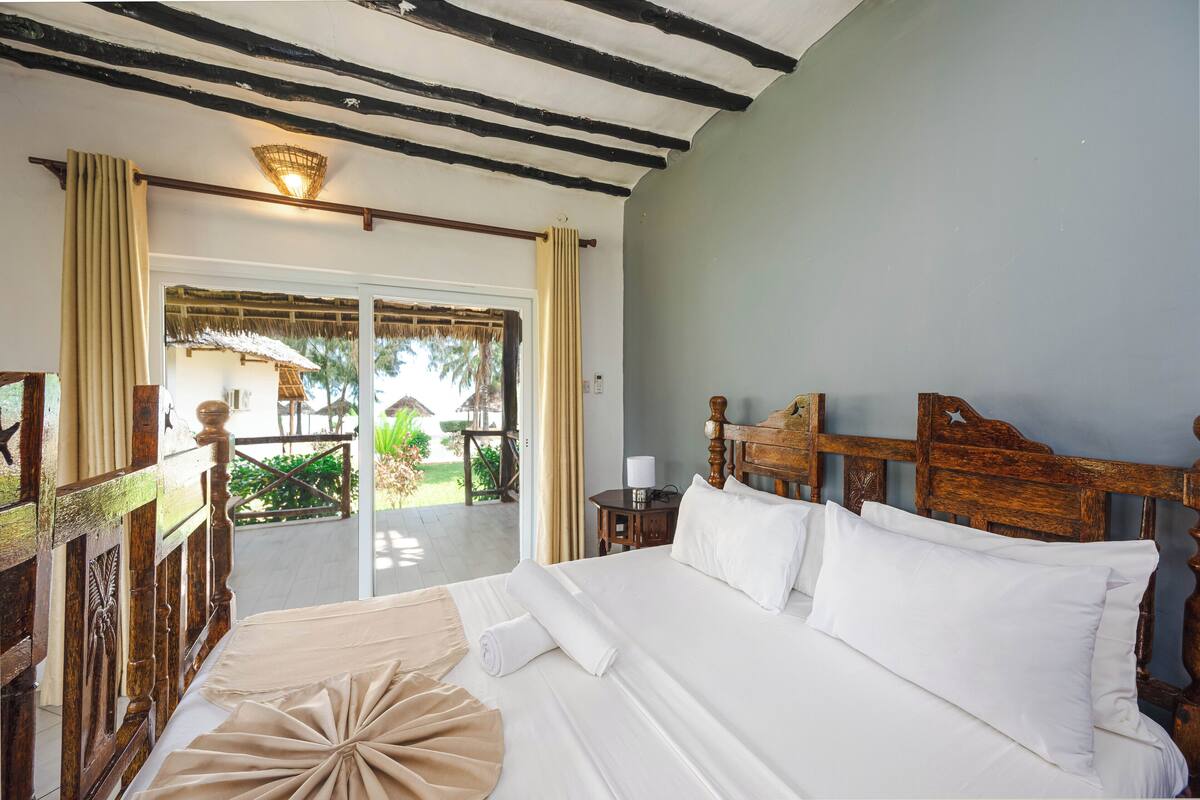 A hotel room with a large bed, wooden headboard, and a view of a garden and outdoor seating area.