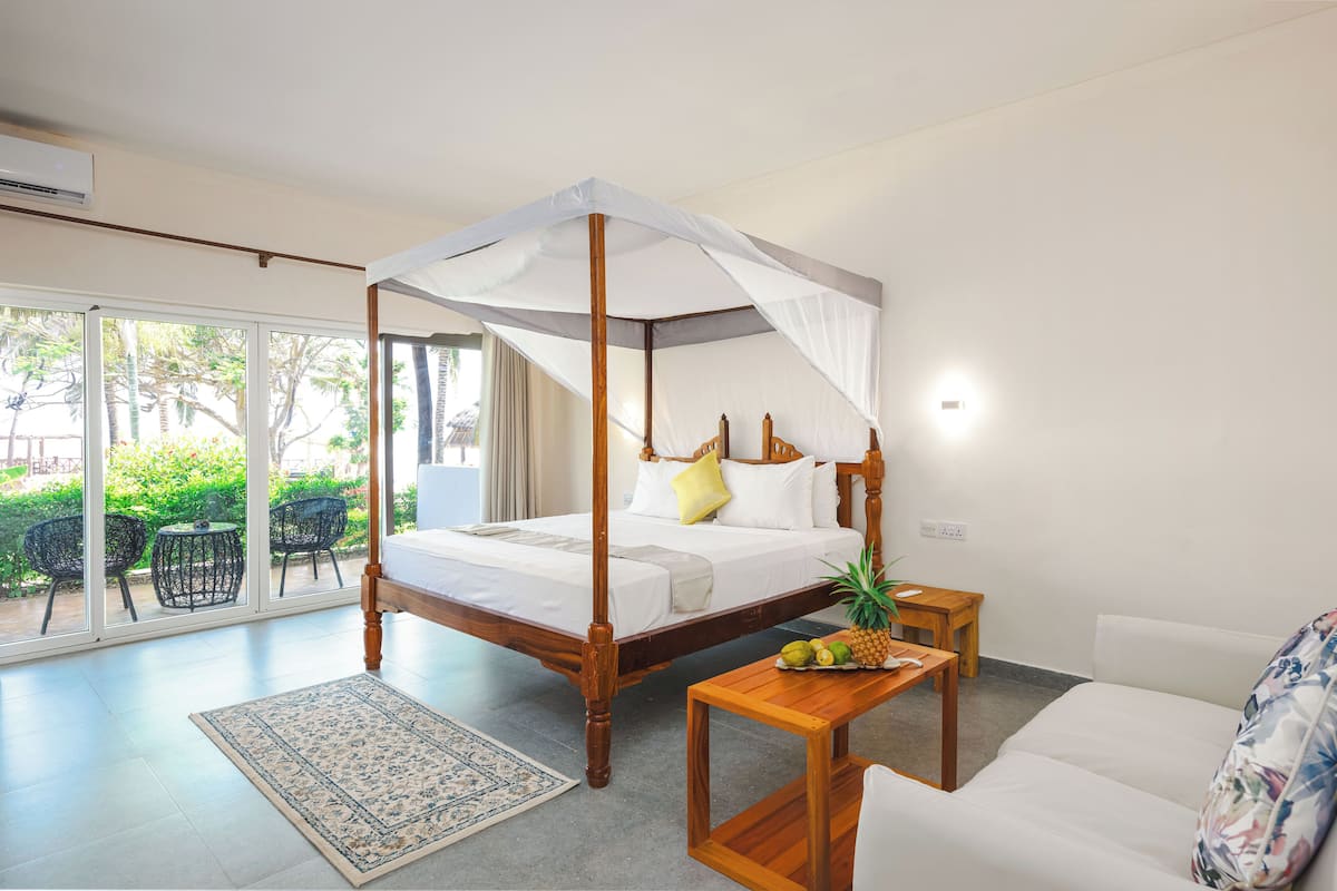 A bedroom with a four-poster bed, a wooden nightstand, a small table with fruits, and a sofa.