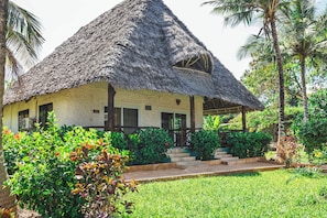 A thatched-roof house with a porch, surrounded by lush greenery and palm trees. - Tanzanite Beach Resort (Nungwi)